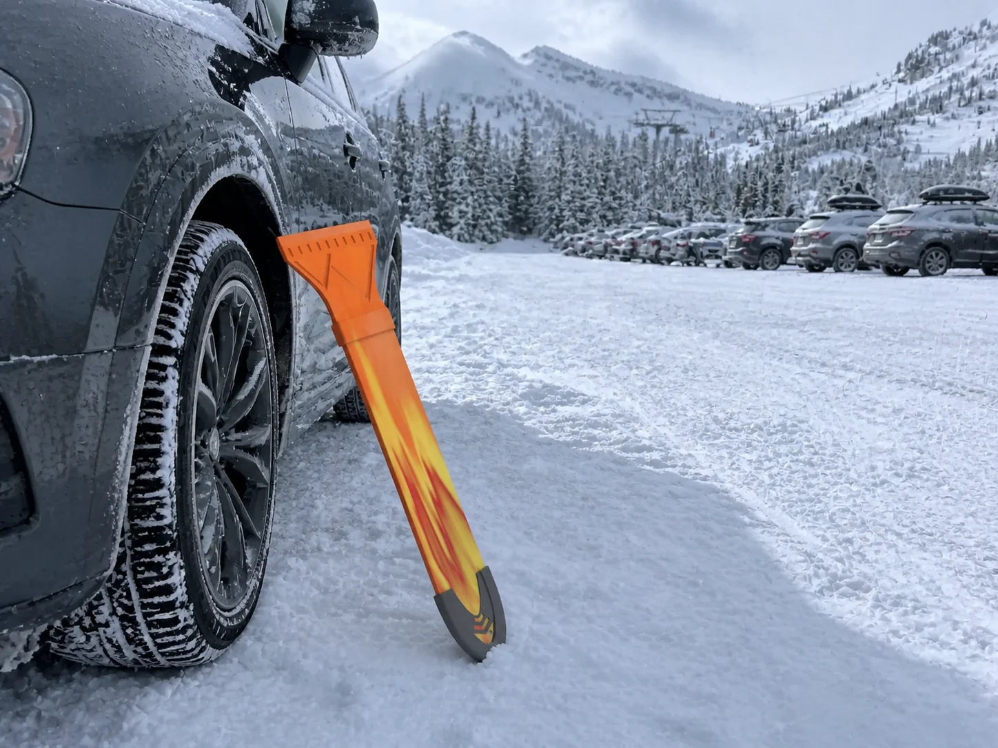 A Ski Scraper resting against a car on a snow-covered driveway.