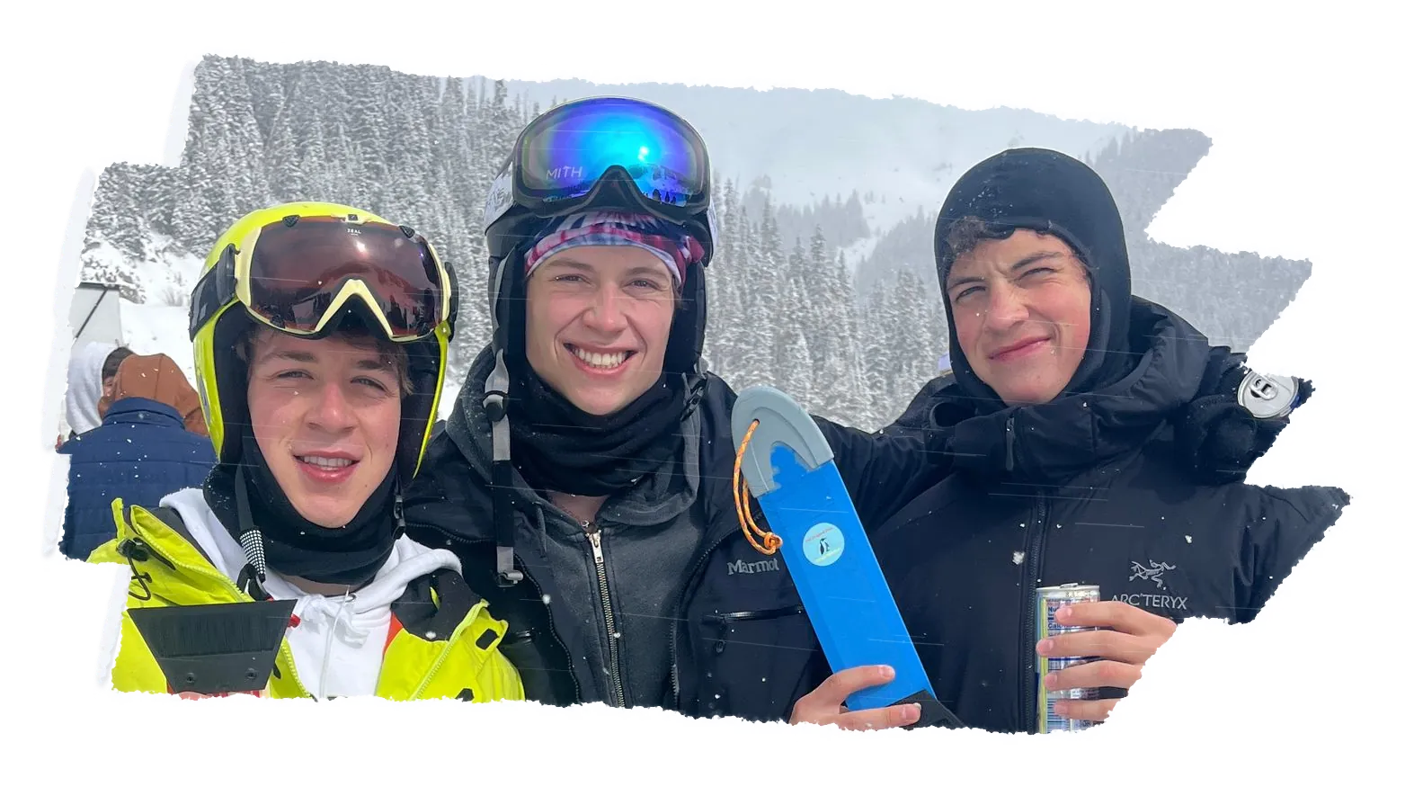 Three skiers in helmets and hoods side by side in the snow, one holding a blue scraper and one a can.