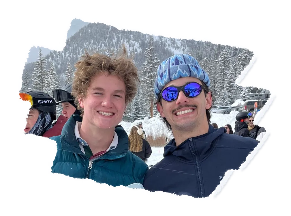 Two snowboarders side by side at a resort base, one in mirrored sunglasses.