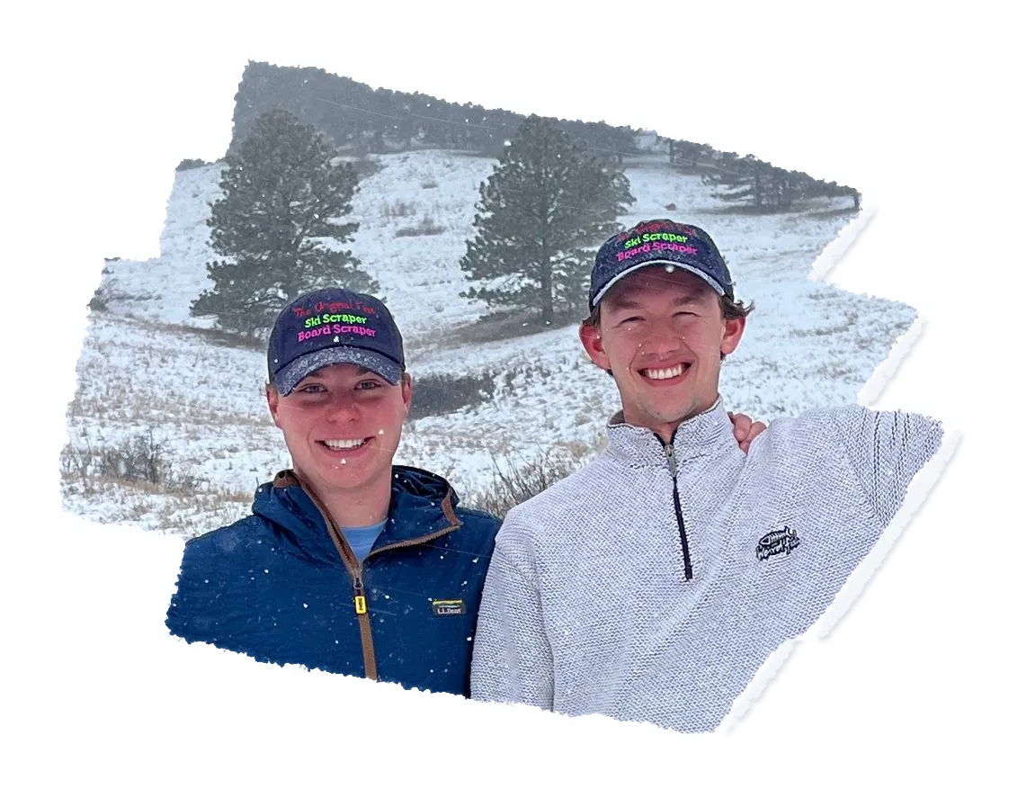 Two people in caps side by side on a snowy hillside, pine trees behind them.