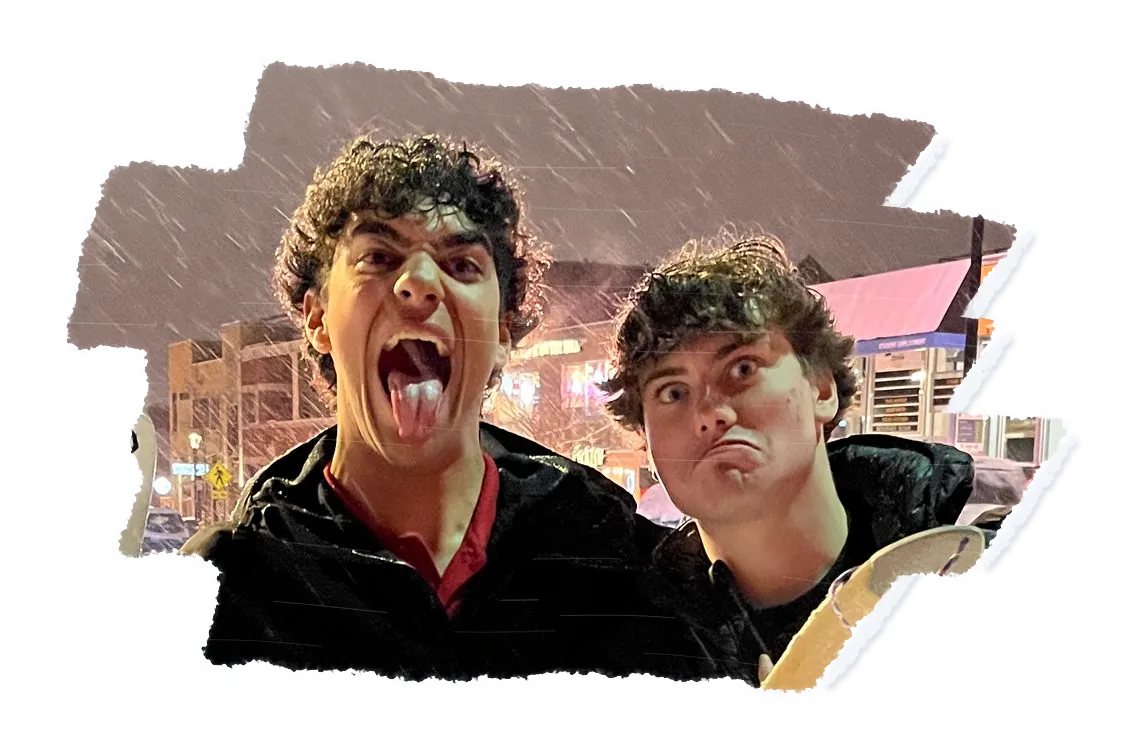 Two people pulling faces at night in falling snow, one with their tongue out, a scraper held up in front.