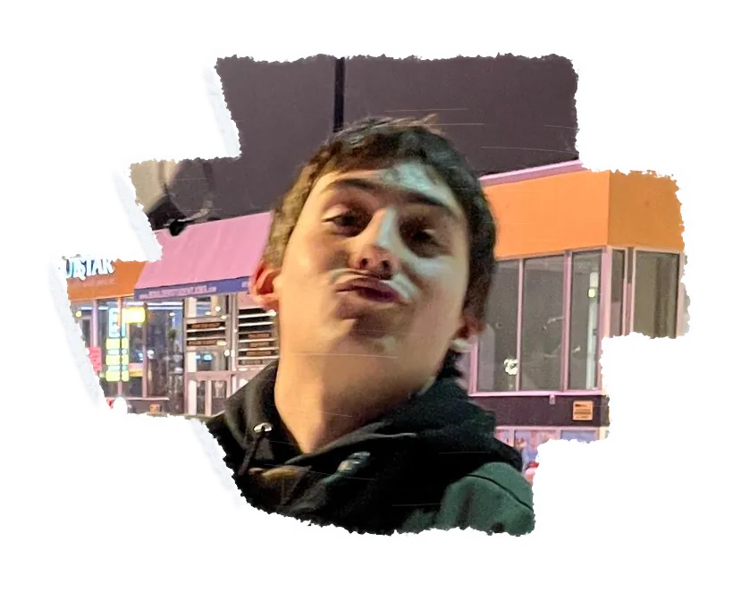 Someone pursing their lips at the camera at night, a lit shop front behind them.