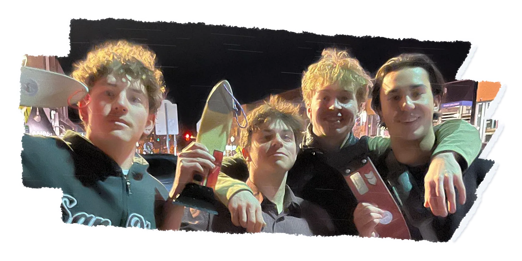 Four people crowded together at night, arms round each other, holding scrapers up to the camera.