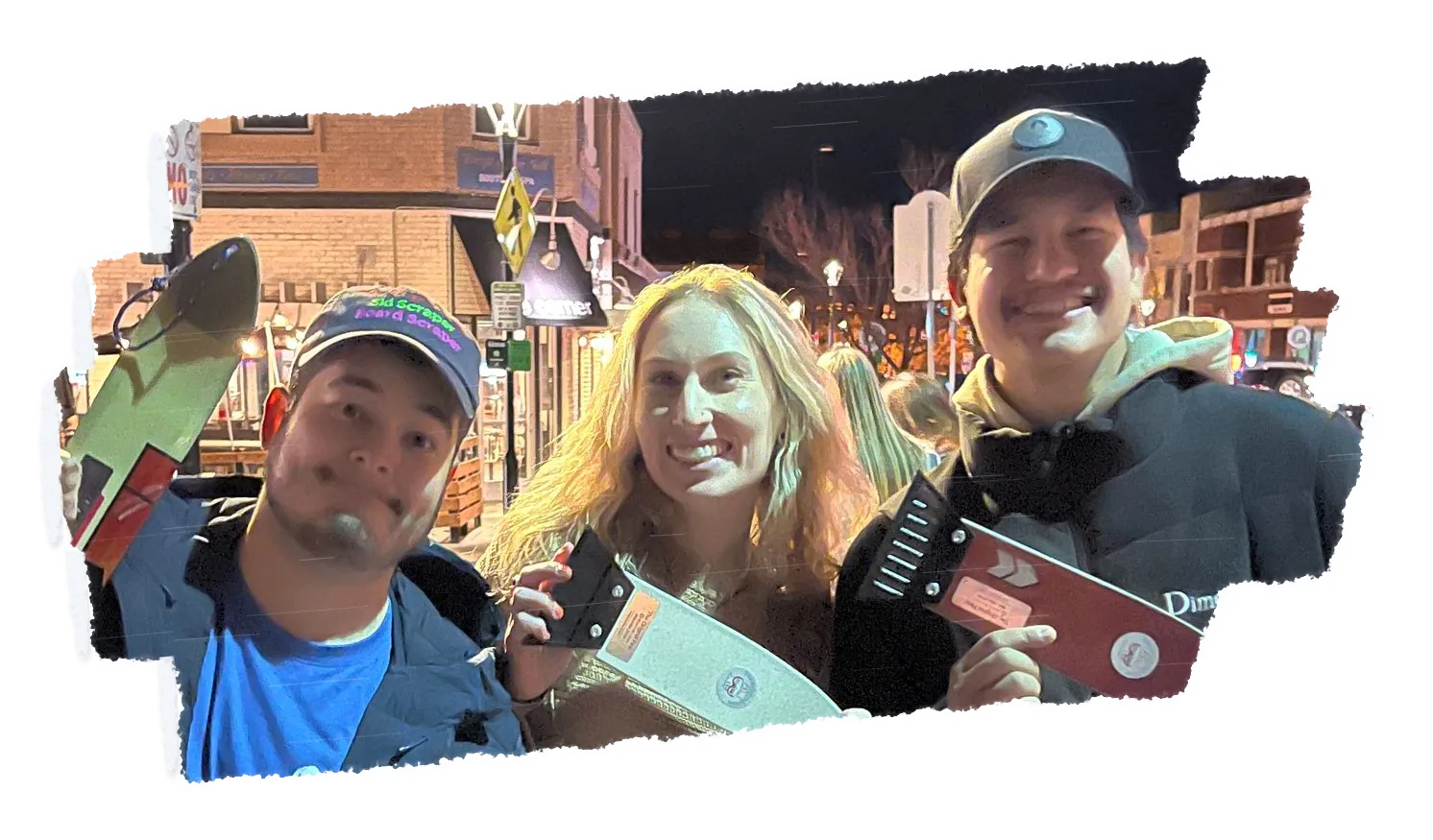 Three people at night, one in a cap, holding scrapers out towards the camera.