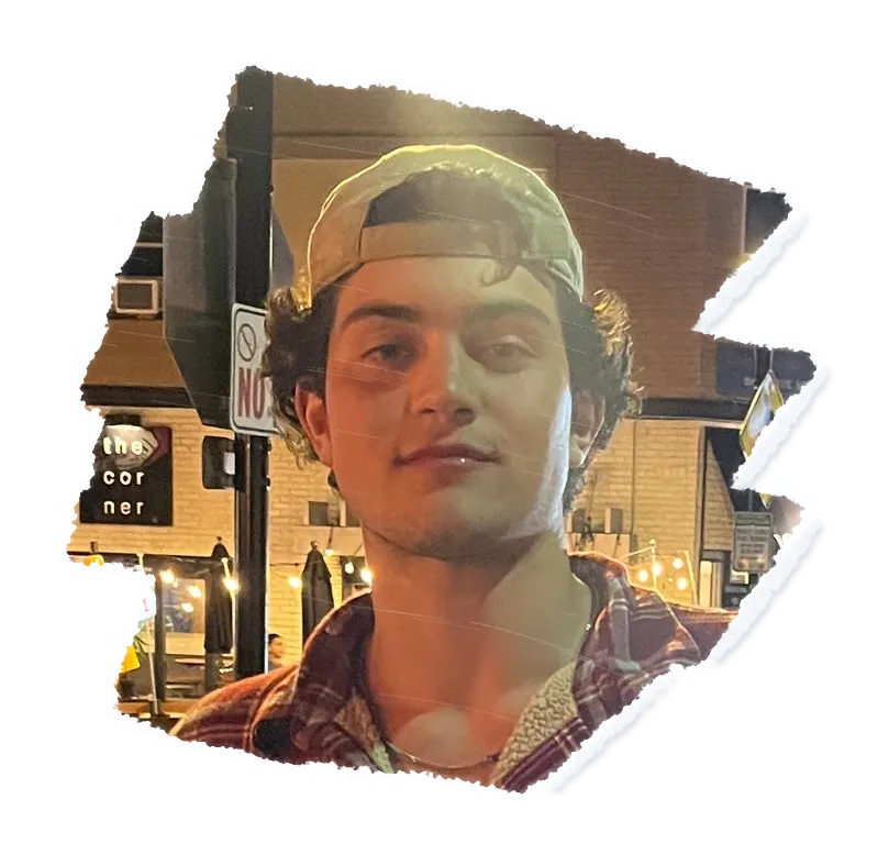 Someone in a backwards cap, lit shop fronts at night behind them.