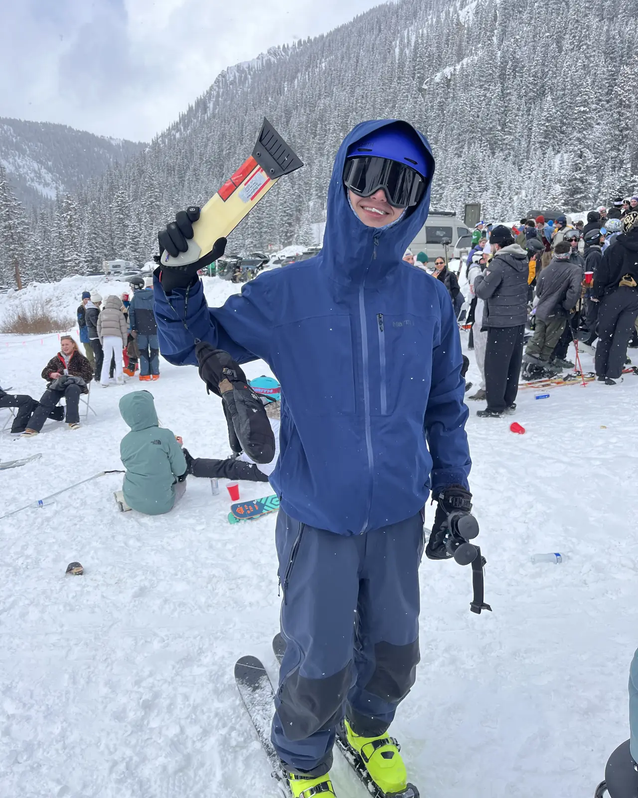 A skier on the snow at a resort base, holding a scraper above their head.
