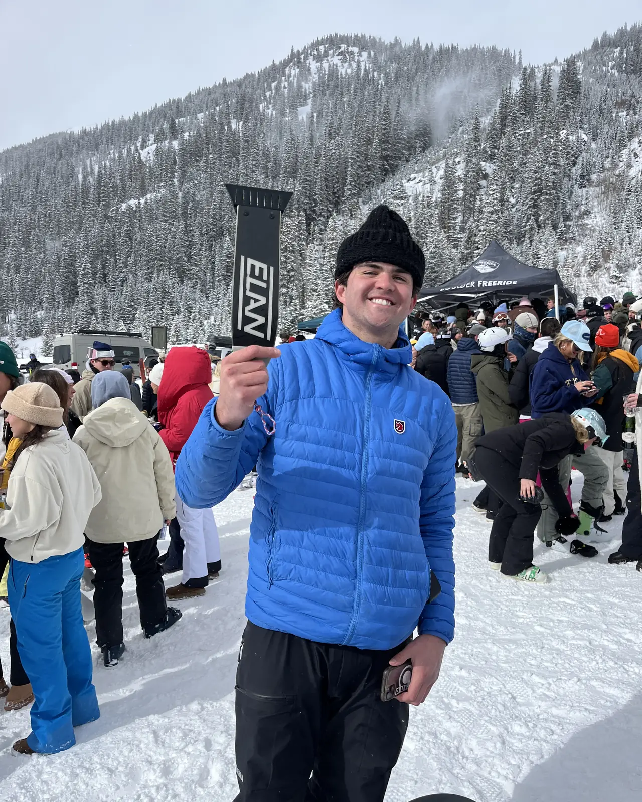 A person in a blue jacket holding a scraper up in front of a crowded resort base.