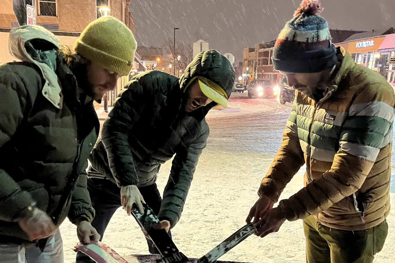 Three people leaning over a table in heavy snow, sorting through scrapers.