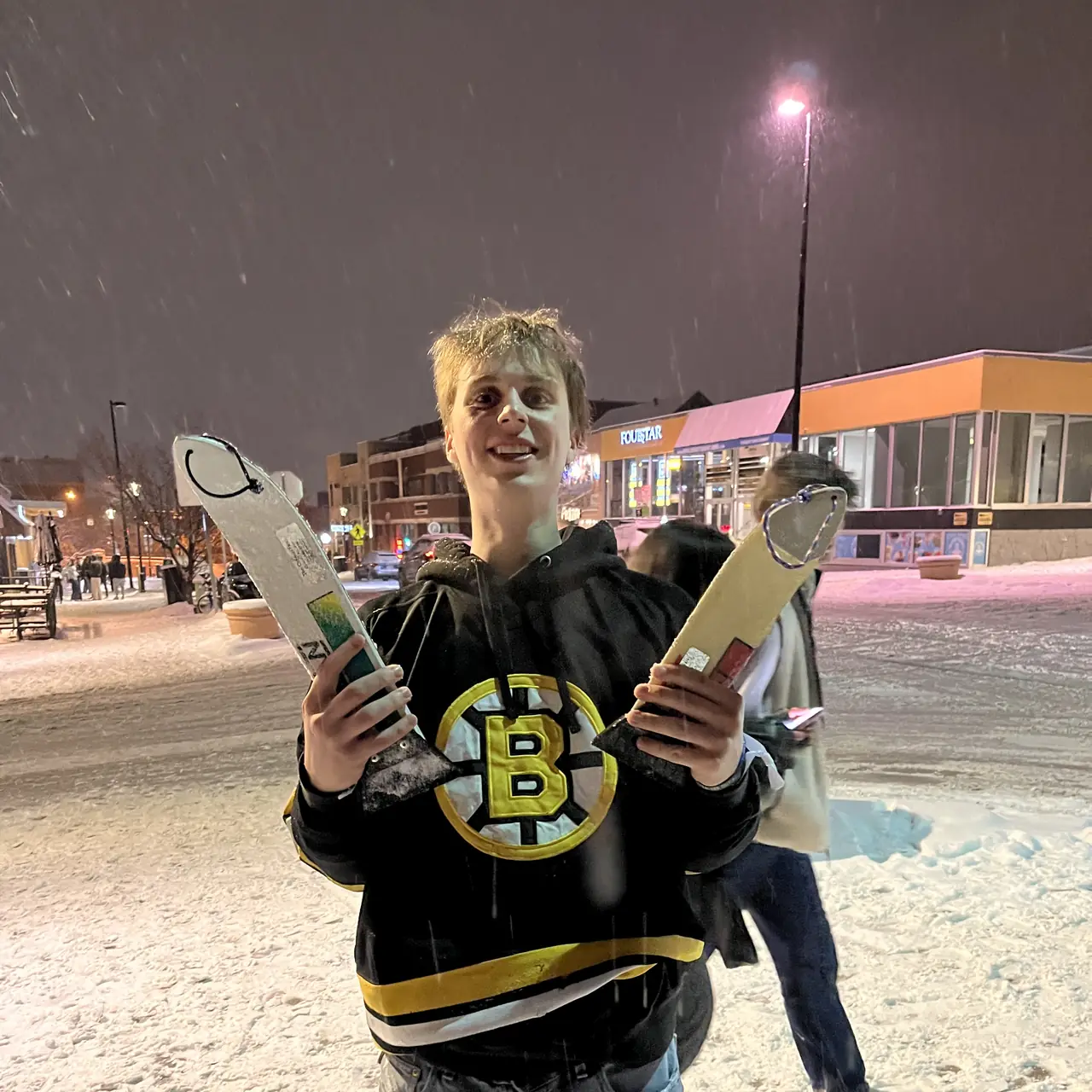 A person in a hockey jersey holding two scrapers crossed in front of them at night.