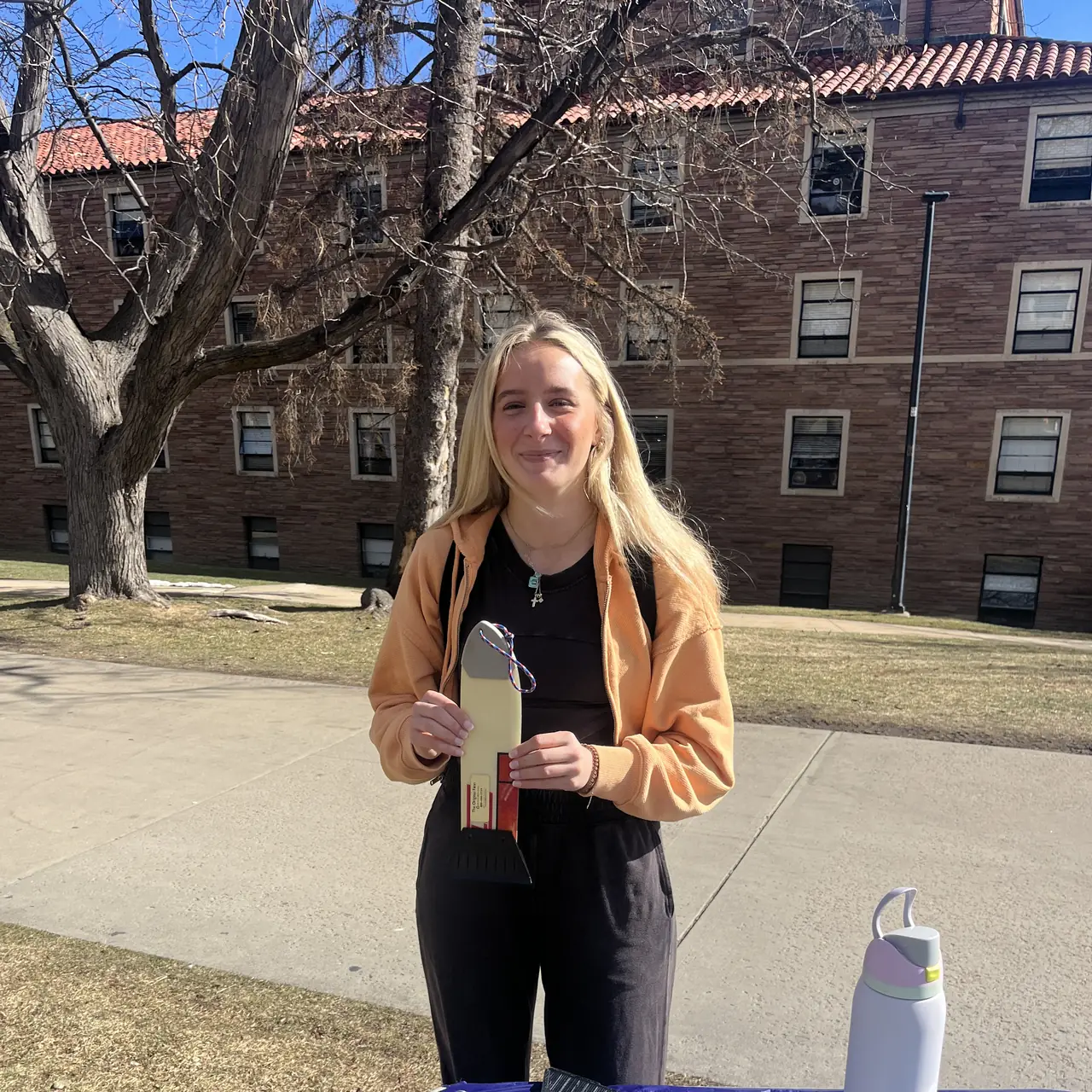 Someone standing behind a trestle table on a campus lawn, holding a scraper in both hands.