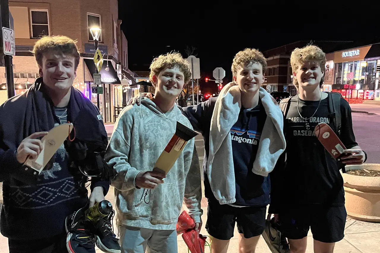 Four people in shorts and hoodies on a night pavement, each holding a scraper.