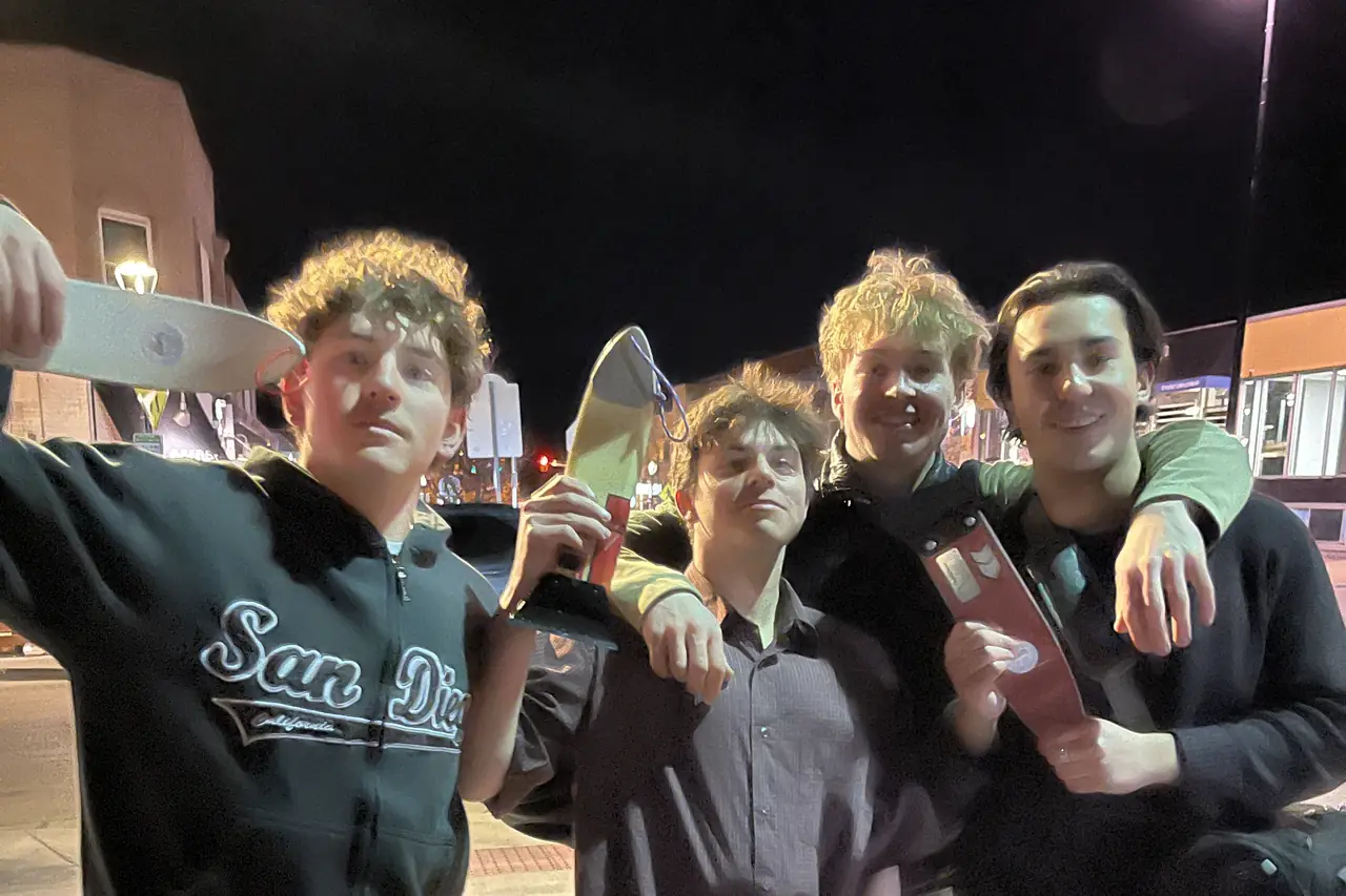 Four people crowded together on a pavement at night, holding scrapers up to the camera.