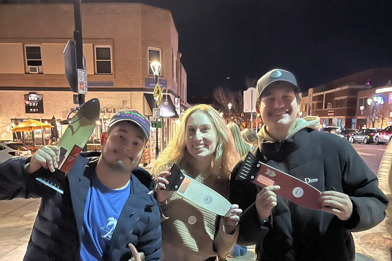 Three people at night holding scrapers out towards the camera.