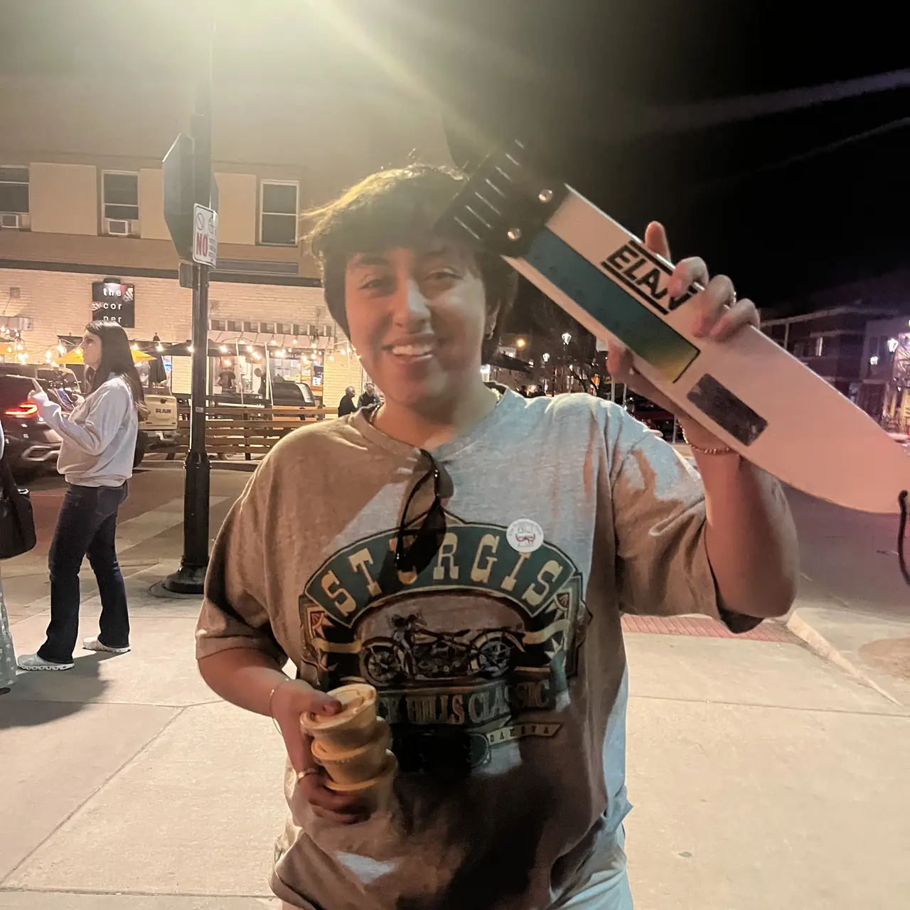 Someone holding a scraper over their shoulder under a street lamp, the light flaring.