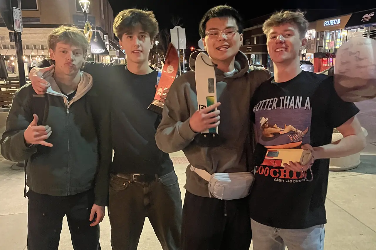 Four people side by side on a pavement at night, one holding a scraper up.