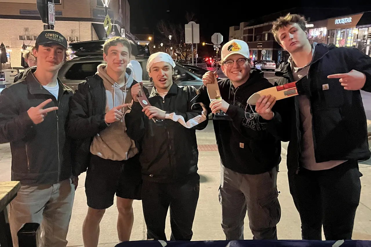 Five people lined up along a pavement at night behind a table, scrapers raised.
