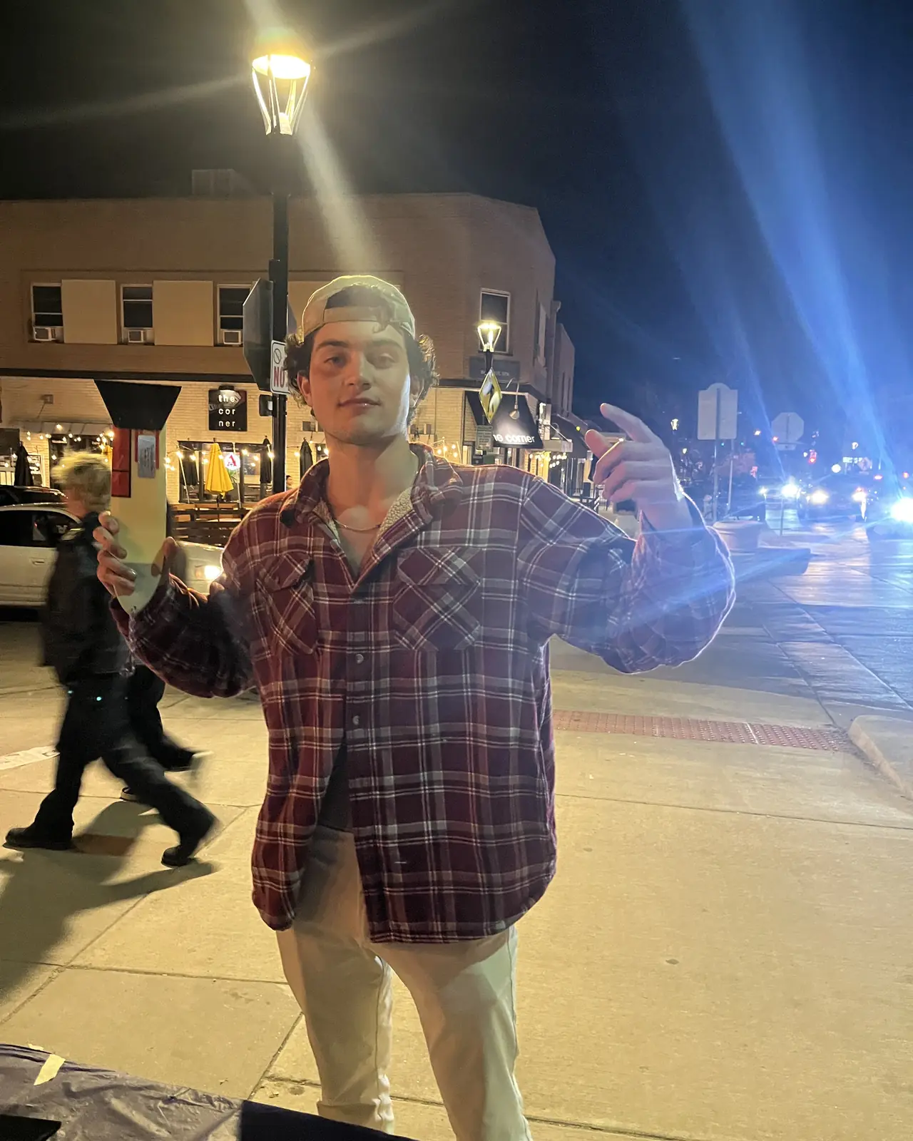 Someone in a plaid shirt on a street corner at night, holding a scraper up.